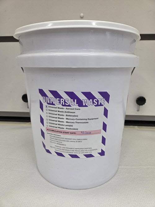 5-gallon white bucket with snap lid and purple and white label.  Label is marked with Universal Waste Aerosols and Accumulation Start Date of 5/1/2025